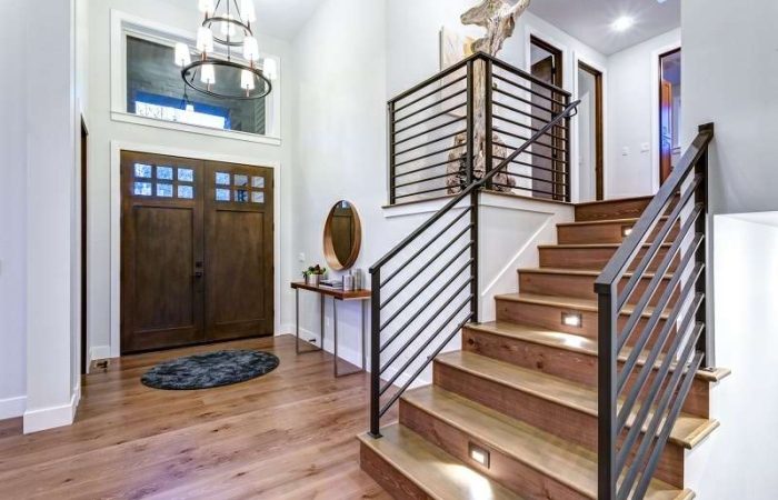 Chic entrance foyer with high ceiling and wide staircase with lights and contemporary railing. New Custom built home interior.